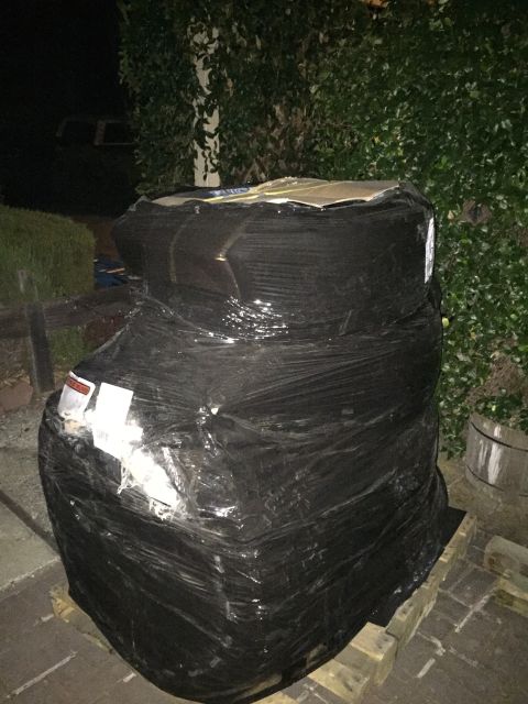 1989 Ford Bronco - A stack of tires is wrapped in plastic and placed on a pallet outdoors at night.