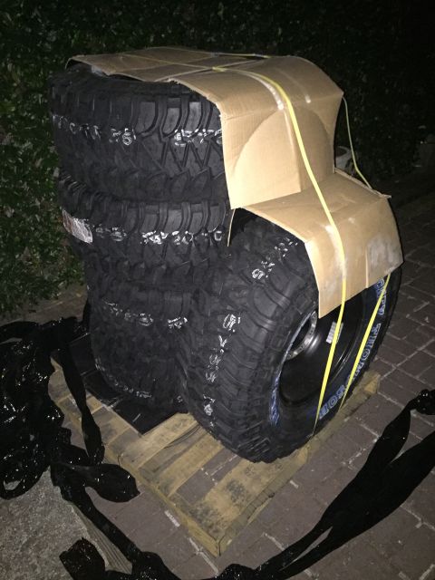 1989 Ford Bronco - A stack of four off-road tires, wrapped in cardboard and secured with yellow straps, sits on a wooden pallet.