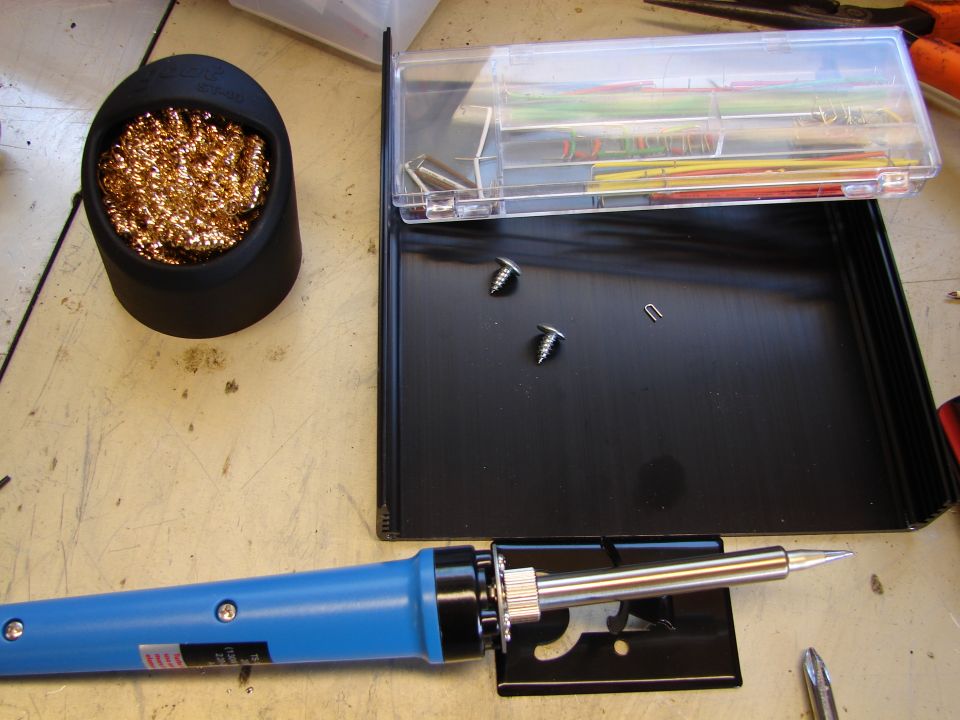 Soldering iron, brass wool tip cleaner, and a box of wires and screws on a workbench