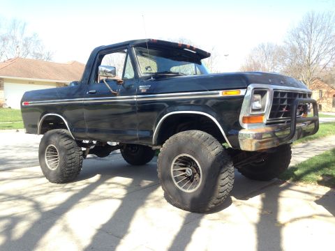 1979 Ford Bronco - This lifted black Ford Bronco is parked on a paved surface in front of a residential house.