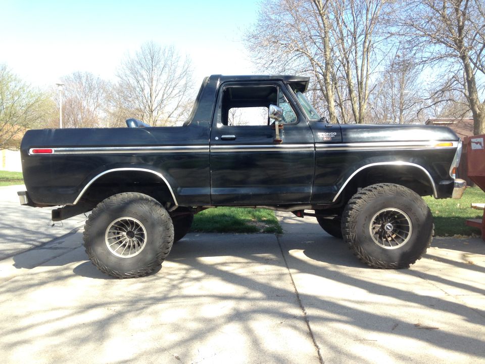 Black 1978 Ford Bronco with large tires, lifted suspension, and chrome trim, viewed from the side