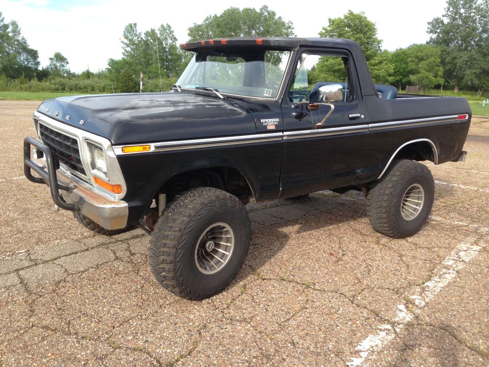 Black 1978 Ford Bronco with a bull bar, lifted suspension, and aftermarket wheels, viewed from the front three-quarter angle
