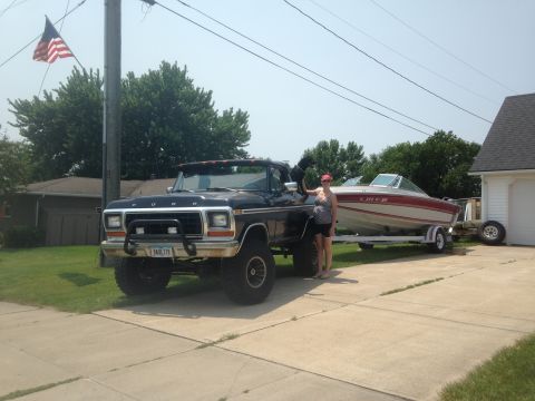 1979 Ford Bronco - A woman and her dog stand next to a lifted black Ford Bronco towing a red and white boat on a trailer.