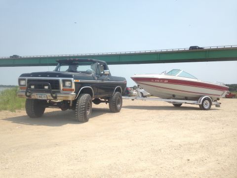 1979 Ford Bronco - A black 1979 Ford Bronco tows a boat on a trailer near a bridge.