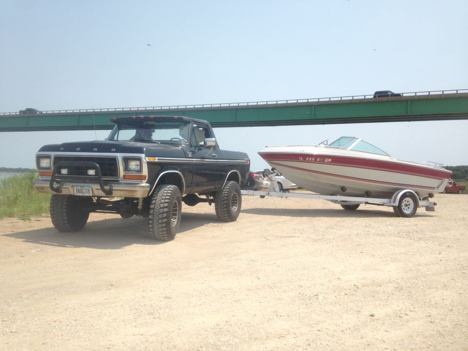 Black 1979 Ford Bronco with bull bar towing a red and white boat on a trailer