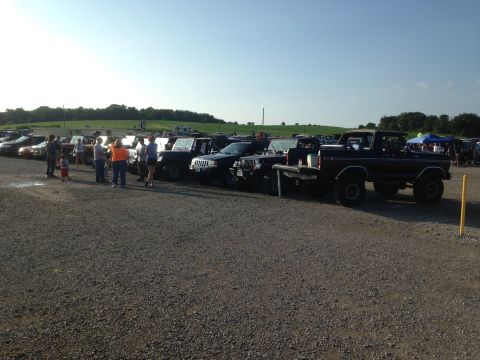 1979 Ford Bronco - Several trucks and SUVs are parked in a gravel lot under a clear sky.