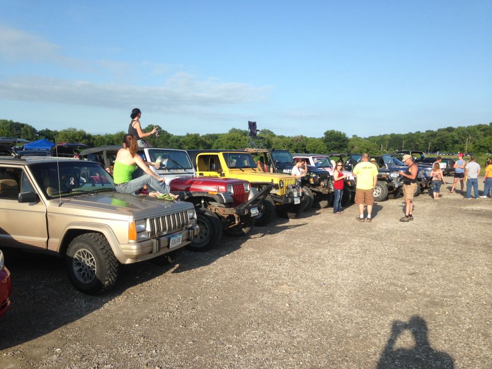 Several Jeeps parked in a lot, some people sitting on hoods