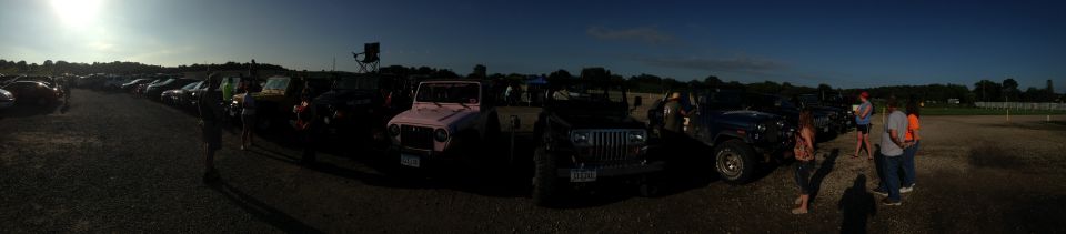 Panoramic view of a parking lot with multiple Jeeps and cars, some people standing around