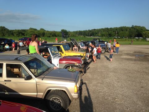 1979 Ford Bronco - A gathering of Jeeps and people in an outdoor lot, with a gold Jeep Cherokee XJ prominently featured in the foreground.