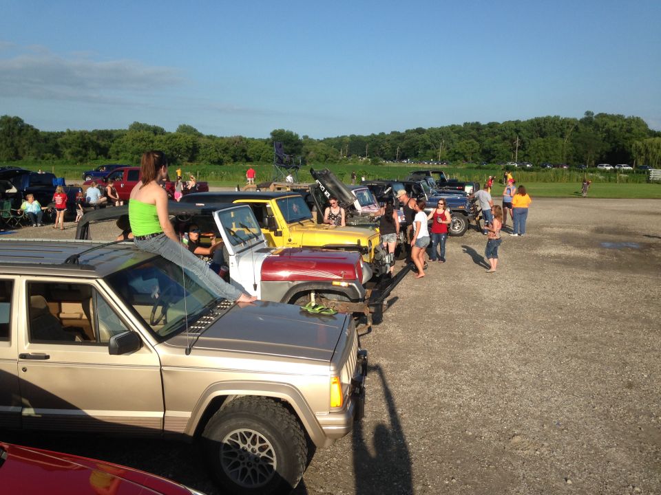Gold Jeep Cherokee XJ parked in a lot with other Jeeps and people