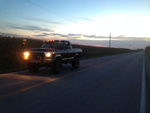 1979 Ford Bronco - 1979 Ford Bronco driving on a rural road at dusk with its headlights on.