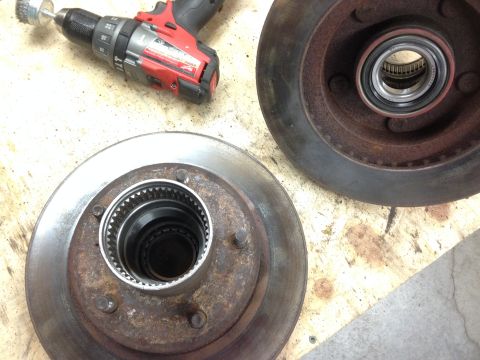 1979 Ford Bronco - A power drill and wire brush sit beside two brake rotors and a vehicle hub assembly on a workbench.