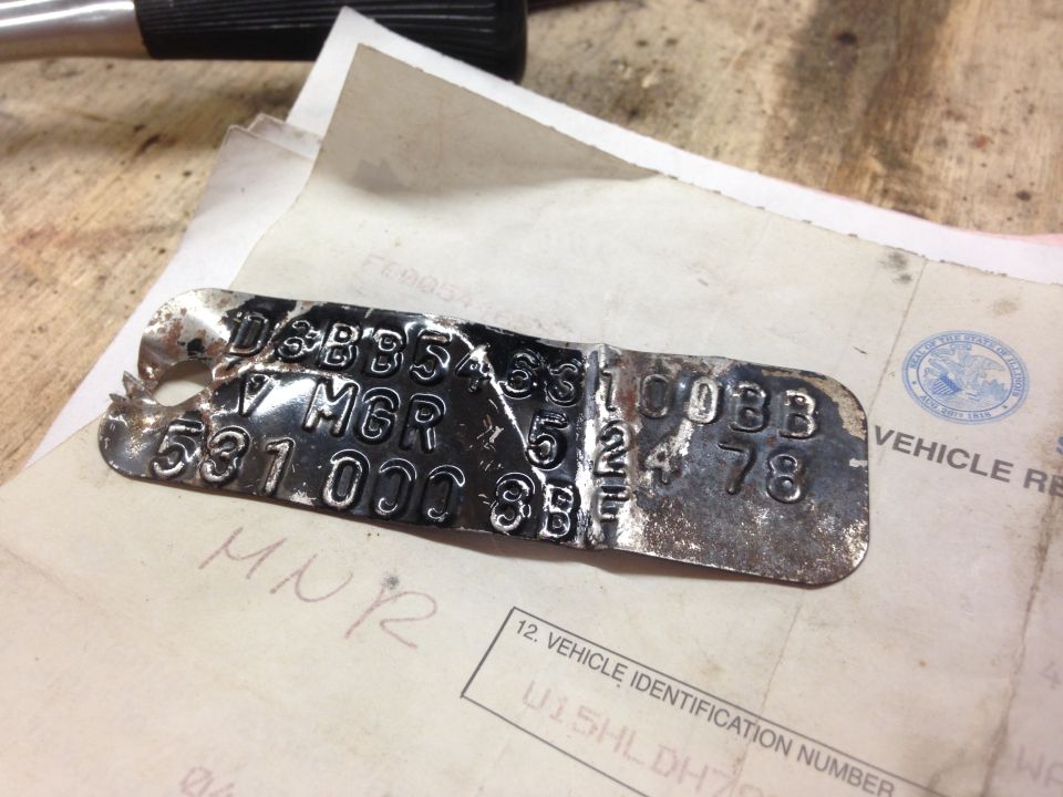 Stamped metal ID tag with worn embossed codes resting on vehicle registration paperwork