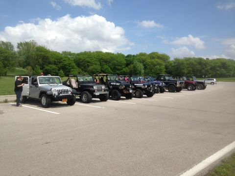 1979 Ford Bronco - A group of Jeeps are parked in a lot on a sunny day with clouds overhead.