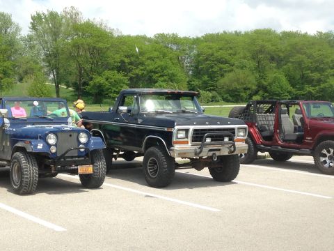 1979 Ford Bronco - Three off-road vehicles are parked in a lot on a cloudy day.