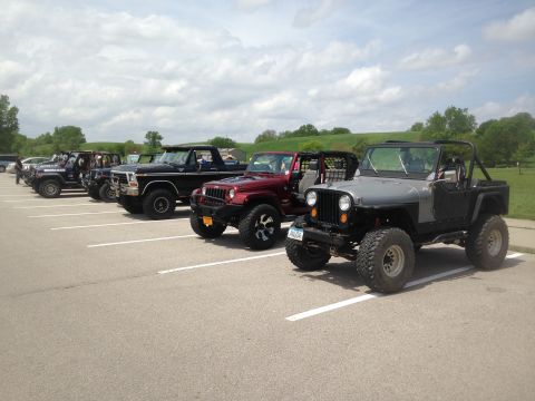 1979 Ford Bronco - A row of off-road vehicles, including a 1979 Ford Bronco, are parked in a lot on a cloudy day.