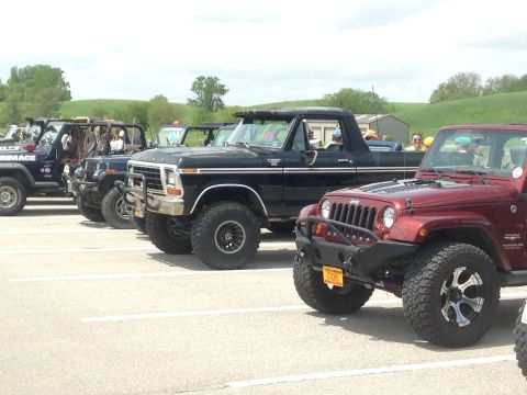 1979 Ford Bronco - Several modified off-road vehicles are parked in a lot on a sunny day.