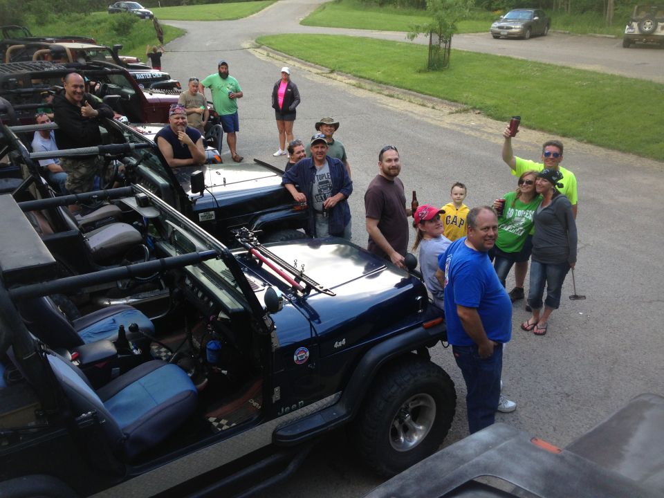 Group of people standing around several Jeeps parked on a road