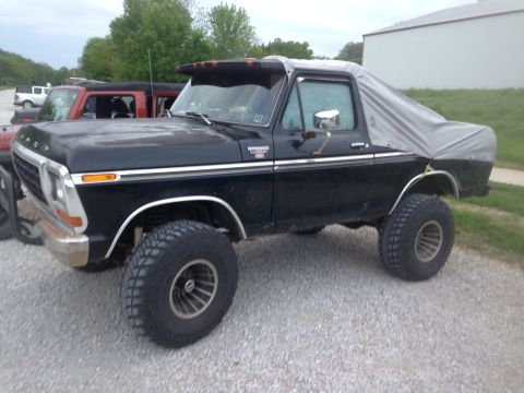 1979 Ford Bronco - This lifted Ford Bronco has a tarp covering its rear section, parked next to other vehicles.