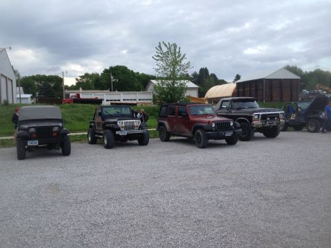 1979 Ford Bronco - A line of off-road vehicles, including a black 1978 Ford truck, are parked on a gravel lot under a cloudy sky.