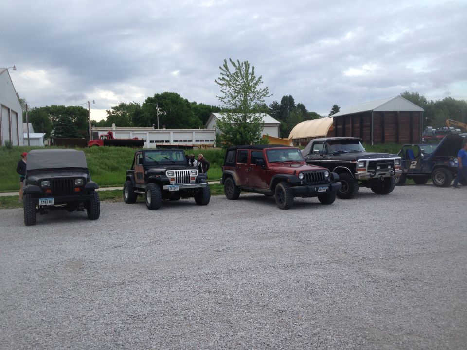 Several off-road vehicles parked on gravel, including a black 1978 Ford F-Series truck with its hood up