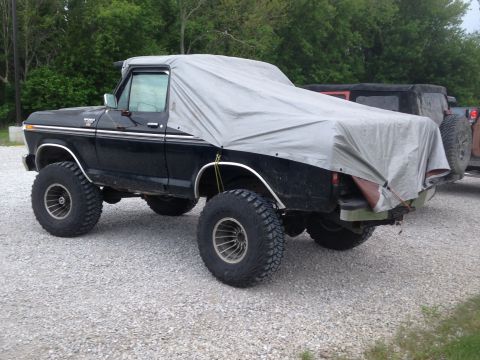 1979 Ford Bronco - This lifted black pickup truck, likely a 1979 Ford, is partially covered by a tarp, revealing its large off-road tires.