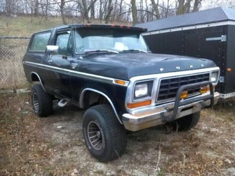 1979 Ford Bronco - This black Ford Bronco is parked outdoors next to a trailer.