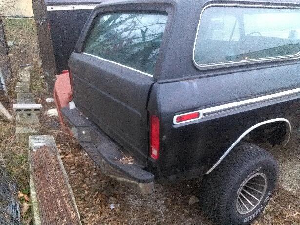 Black 1978 Ford Bronco rear quarter panel with chrome trim and a red taillight, parked next to a black trailer