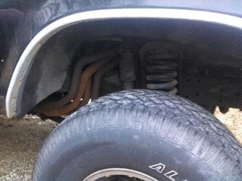 1979 Ford Bronco - The image shows a close-up view of the suspension and exhaust system of a vehicle, focusing on the front tire and wheel well.