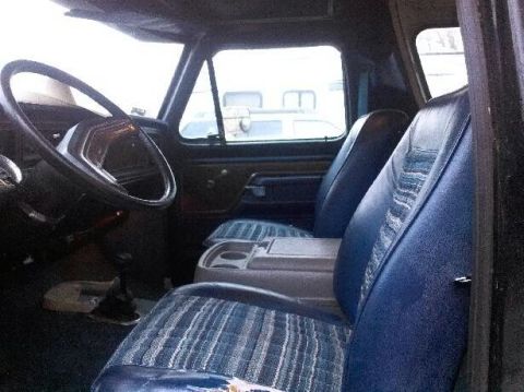 1979 Ford Bronco - The interior of the vehicle shows blue fabric seats with a striped pattern and a gray center console.