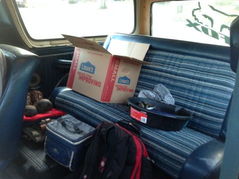 1979 Ford Bronco - The interior of a vehicle shows a Lowe's box and other items on the blue striped seat.