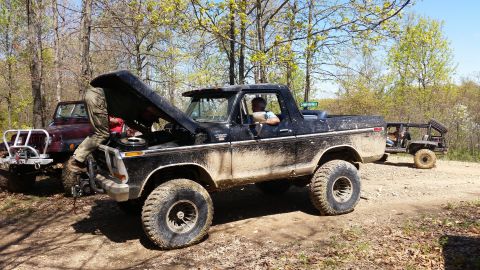 1979 Ford Bronco - A group of off-road vehicles are seen in a wooded area, with one Bronco undergoing maintenance.