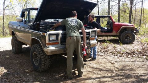 1979 Ford Bronco - Two men inspect the engine of a lifted 1978 Ford Bronco, with a red Jeep visible in the background.