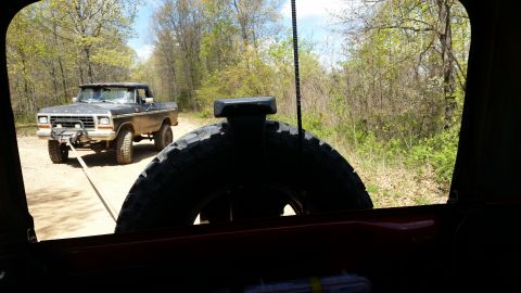 1979 Ford Bronco - A 1979 Ford F-Series pickup truck, equipped with a winch, is being towed along a dirt road through a wooded area.