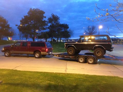 1979 Ford Bronco - A black 1978 Ford Bronco is transported on a trailer behind a red pickup truck under a twilight sky.