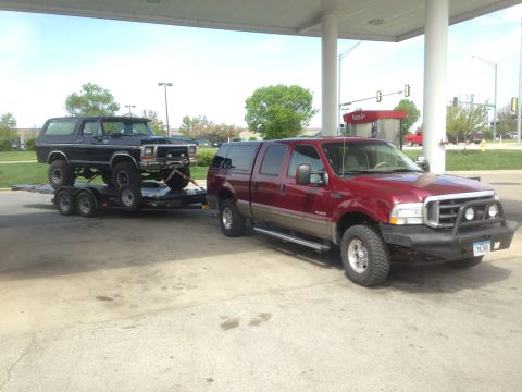 1979 Ford Bronco - A black 1978 Ford Bronco is transported on a trailer, towed by a red Ford Excursion at a gas station.