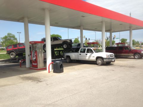 1979 Ford Bronco - Multiple trucks and SUVs are parked at a gas station, some on trailers.