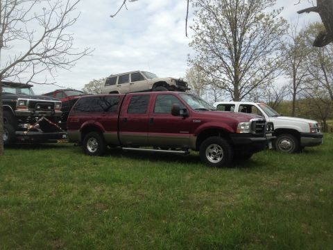 1979 Ford Bronco - A red crew cab pickup truck with a camper shell is parked in a grassy area alongside other vehicles.
