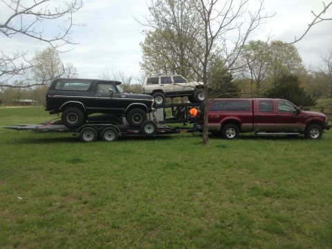 1979 Ford Bronco - Multiple vehicles are loaded onto and beside a trailer, including a Bronco, SUV, and pickup truck.