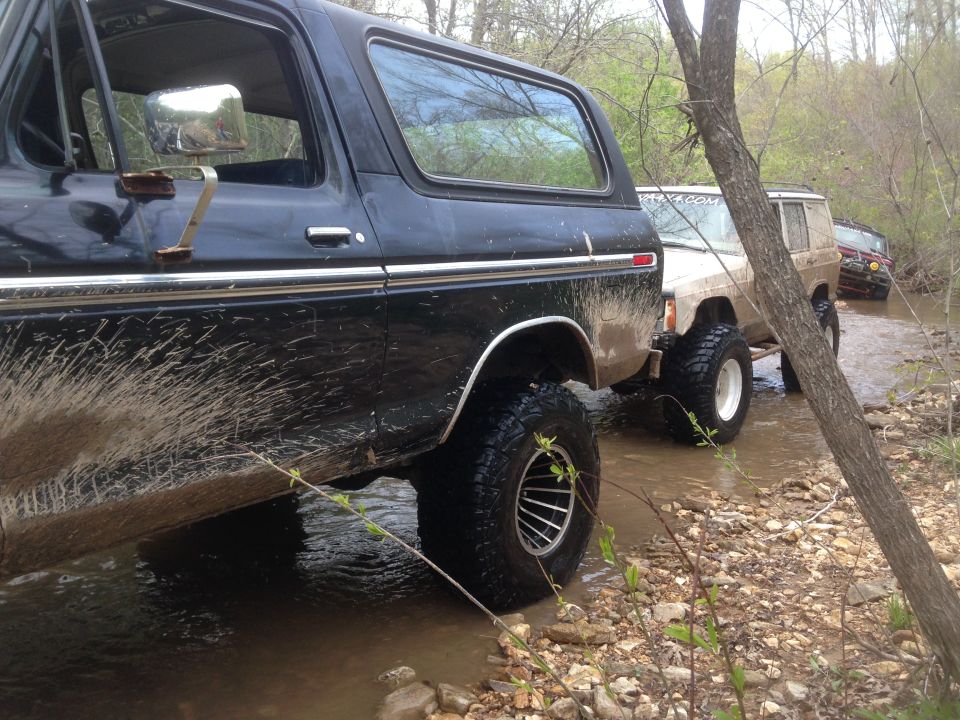 Black Ford Bronco driving through a creek with other SUVs behind it