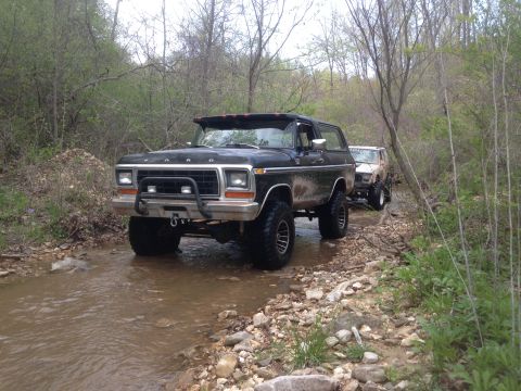 1979 Ford Bronco - A black 1979 Ford Bronco navigates a rocky stream bed, followed by another off-road vehicle.
