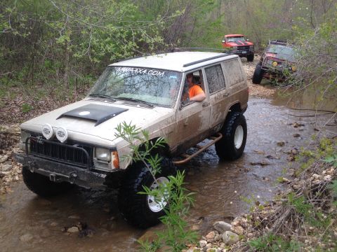 1979 Ford Bronco - Multiple off-road vehicles navigate a shallow creek bed surrounded by trees.