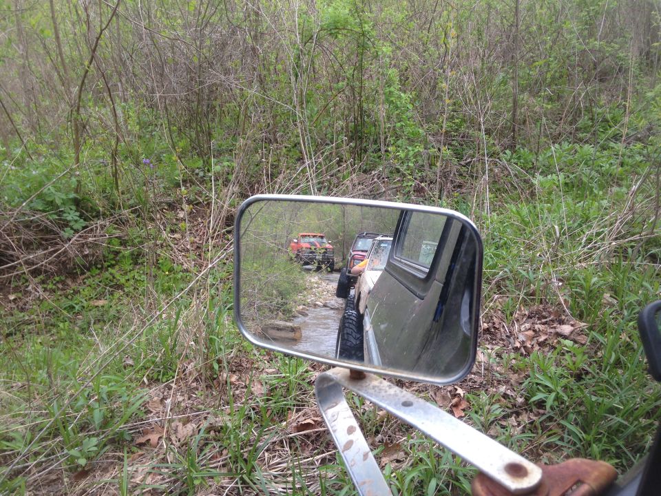 Side mirror view of off-road vehicles driving through a stream