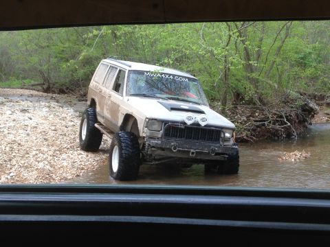 1979 Ford Bronco - White SUV navigates through a water crossing, kicking up spray.