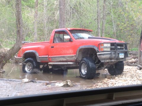 1979 Ford Bronco - A red pickup truck sits outside in the rain, its tires and front end visible.