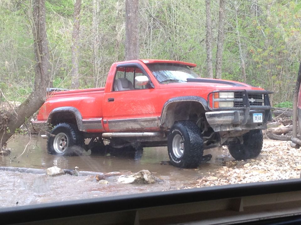 Red pickup truck with off-road tires parked outside in the rain