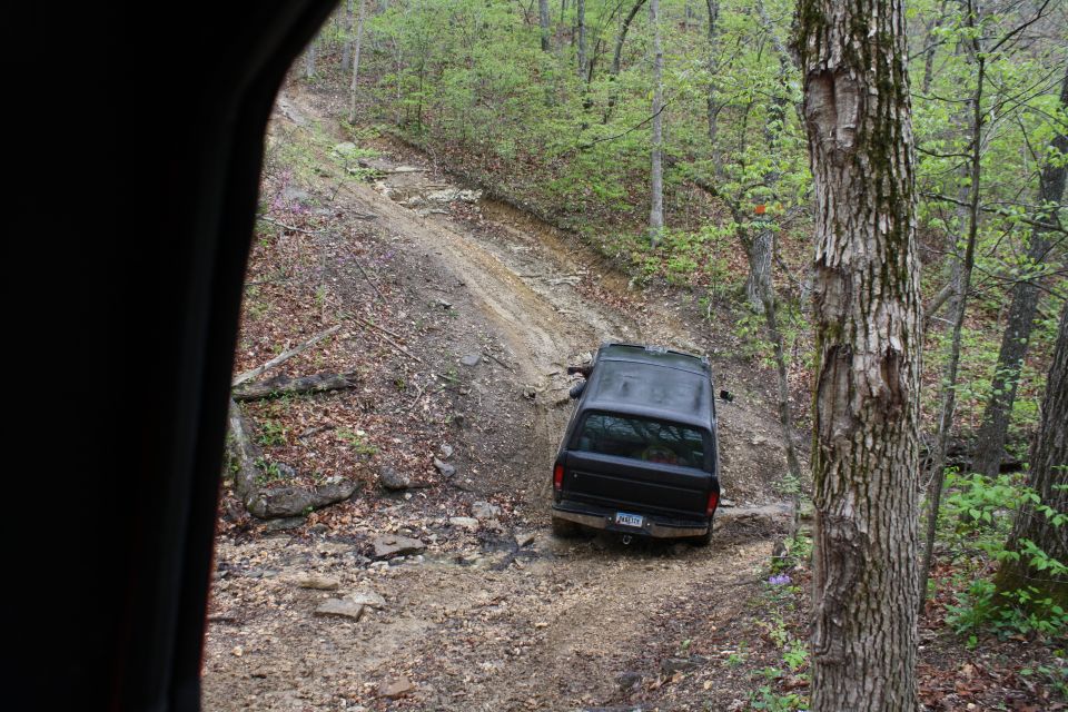 Black 1979 Ford Bronco driving on a dirt trail in a wooded area