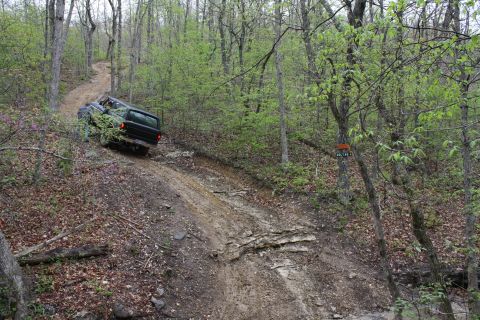1979 Ford Bronco - A 1979 Ford Bronco navigates a challenging muddy and rocky incline on a wooded trail.