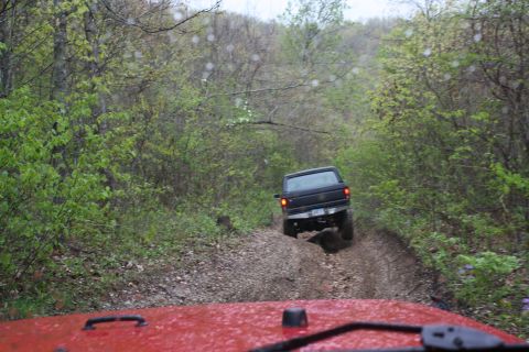 1979 Ford Bronco - Two vehicles navigate a wet, off-road path through a dense forest.