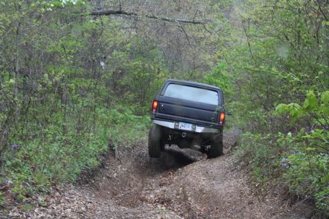 1979 Ford Bronco - A black SUV navigates a challenging off-road trail surrounded by dense foliage.